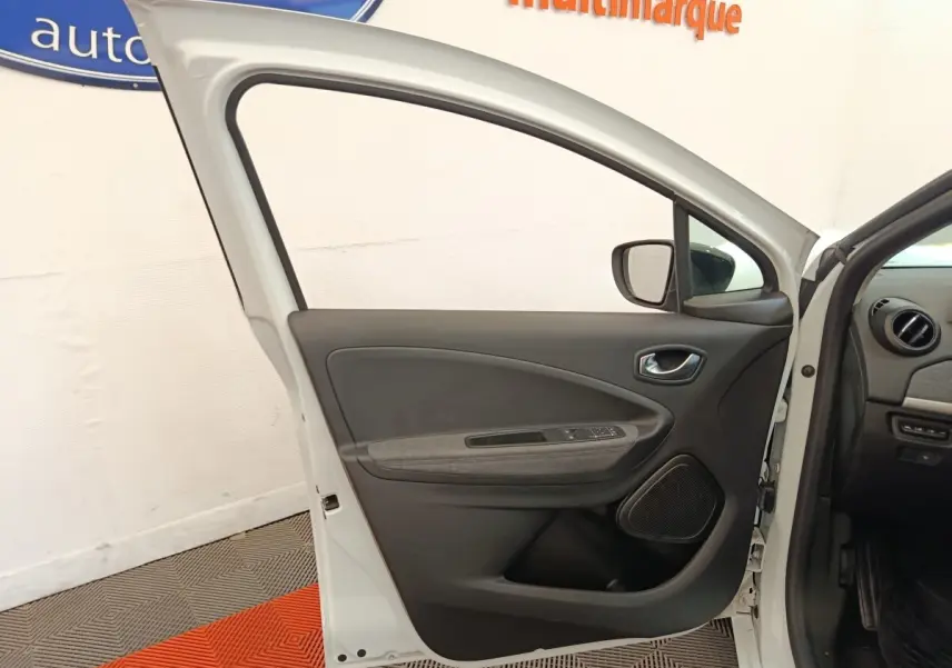 Vue intérieure de la porte avant gauche blanche de la Renault ZOE 2023 avec panneau noir et gris, et commandes électriques.