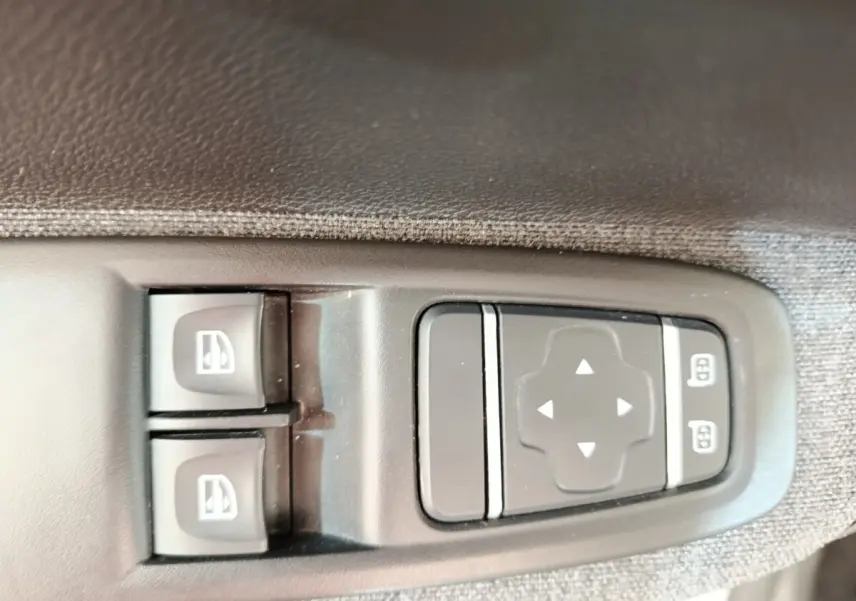 Gros plan sur les commandes électriques des vitres et des rétroviseurs sur la porte côté conducteur d’une Renault ZOE blanche.