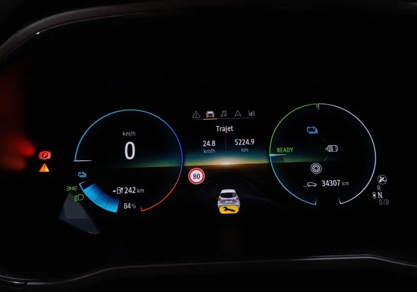 Tableau de bord numérique de Renault ZOE blanc, affichage multifonctions avec vitesse, autonomie et alertes visibles.