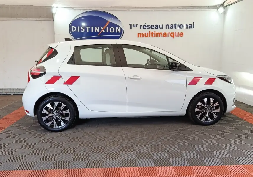 Profil droit de la Renault ZOE blanche 2023 avec bandes rouges sur ailes avant et arrière, jantes noires et grises.
