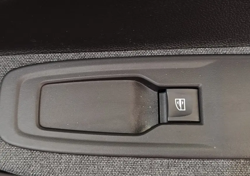 Gros plan sur le bouton de commande électrique de la vitre, intégré dans la garniture intérieure grise de la Renault ZOE blanche.