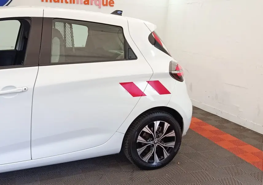 Vue latérale arrière droite d'une Renault ZOE blanche avec marquage rouge sur l'aile arrière et jantes noires.