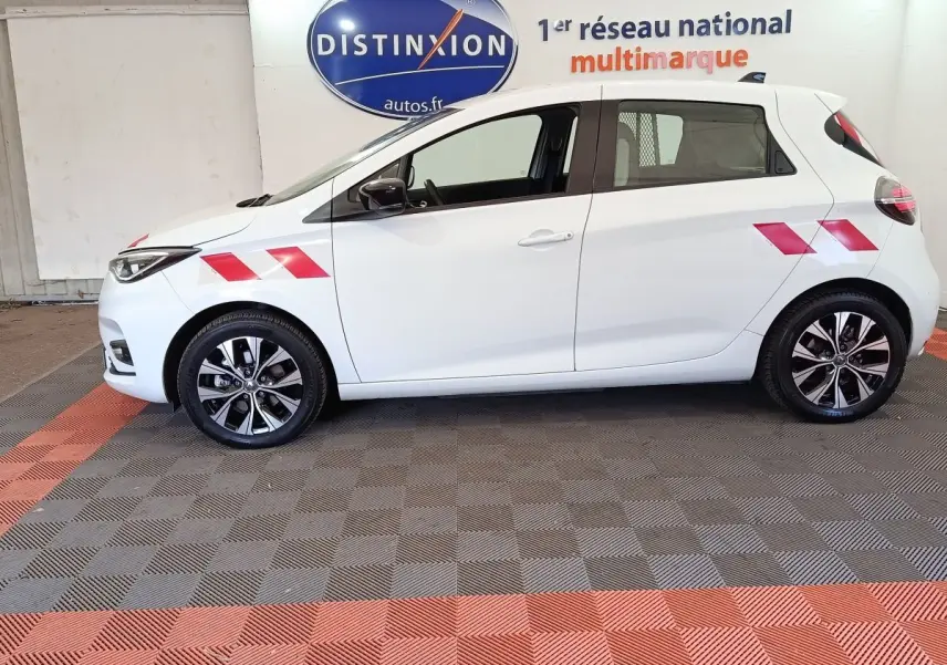 Profil côté gauche de la Renault ZOE blanche 2023 avec marquages rouges et jantes alliage noires et argentées.