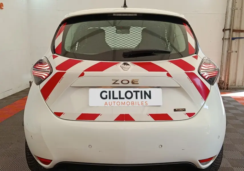 Vue arrière d'une Renault ZOE blanche 2023 avec bandes rouges diagonales de sécurité et feux arrière LED allumés.