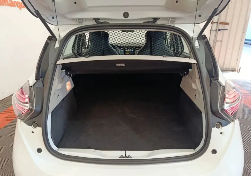 Coffre ouvert vu de l'arrière d'une Renault ZOE blanche avec séparation grillagée et banquette avant visible.