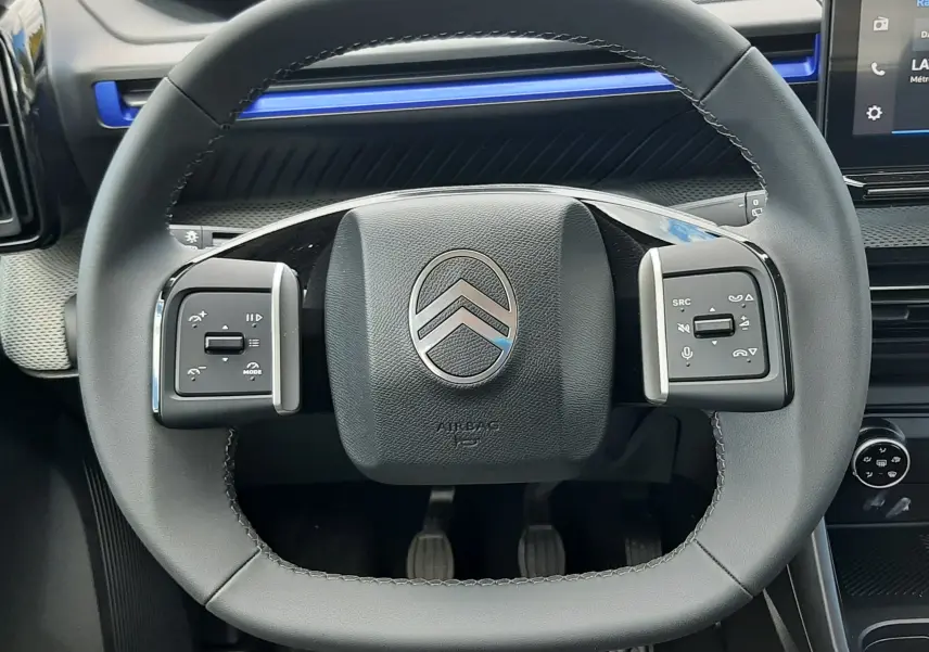 Vue rapprochée du volant noir de la Citroën C3 Turbo 100ch Plus 2026, avec tableau de bord et bandeau bleu Monte Carlo en arrière-plan.