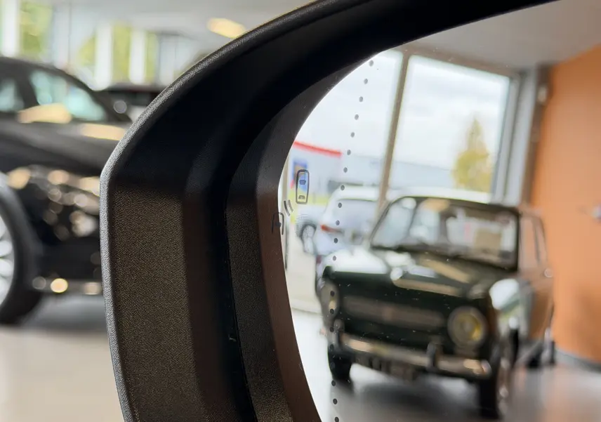 Rétroviseur intérieur d’un Renault Austral E-Tech gris schiste avec toit noir, vue floue d’un véhicule ancien en arrière-plan.