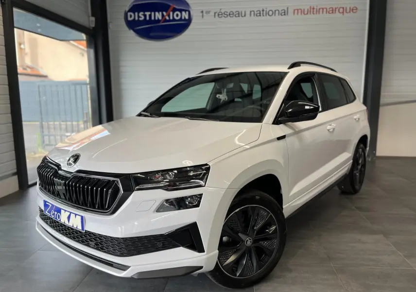 SUV SKODA KAROQ blanc en 3/4 avant droit avec calandre noire et jantes alliage noires dans un showroom.