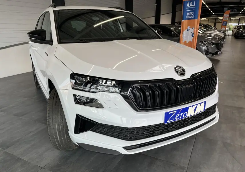 Vue 3/4 avant d'un SUV Skoda Karoq blanc avec calandre noire et phares LED, roues braquées à gauche en showroom.