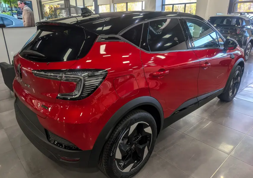 Vue 3/4 arrière droite d'un Renault Captur E-TECH hybride rouge flamme avec toit noir brillant en showroom.