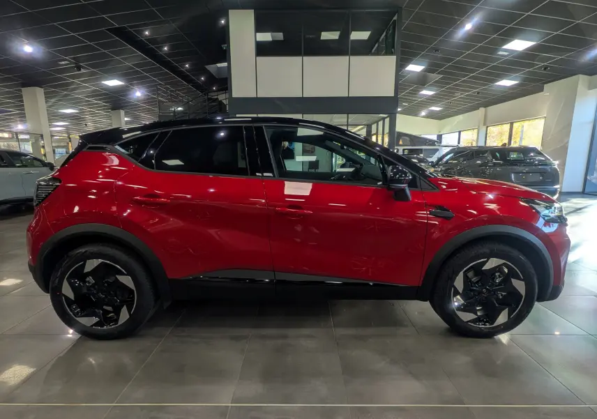 Renault Captur E-TECH 160 ch en profil côté gauche, rouge flamme avec toit noir et jantes noires stylisées.