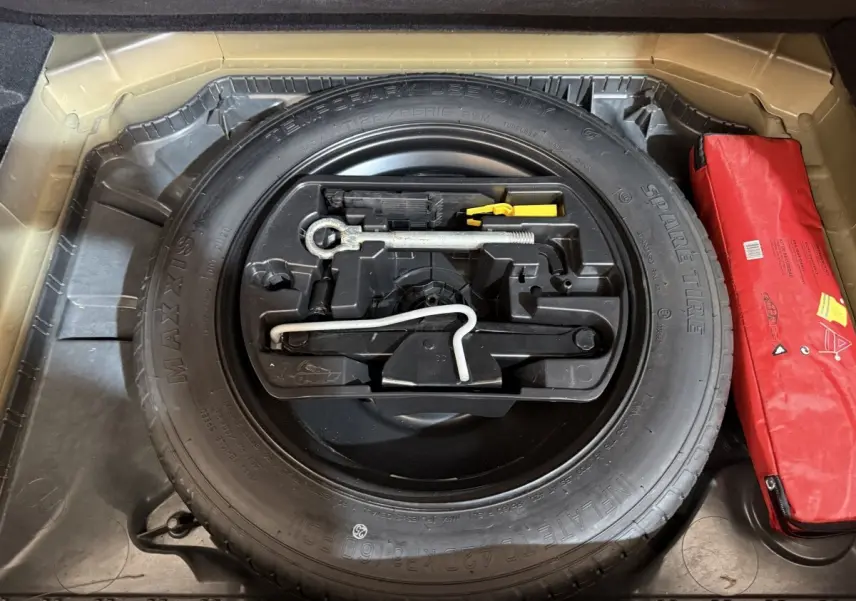 Vue rapprochée de la roue de secours noire et des outils de bord dans le coffre d'une Citroën C4 Spacetourer noire.