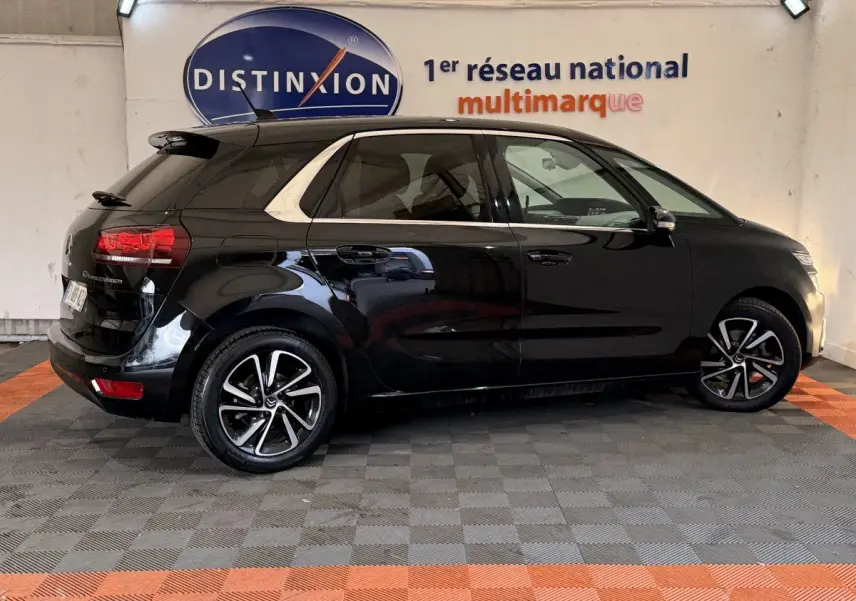 Vue latérale droite d'une Citroën C4 Spacetourer noire avec jantes alliage et toit noir brillant en intérieur showroom.