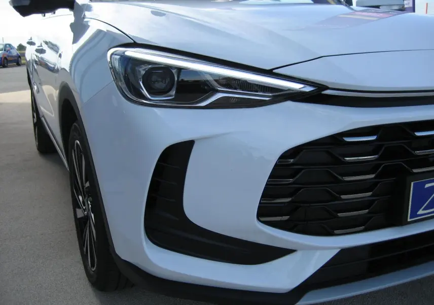 Vue 3/4 avant gauche du MG ZS blanc, mettant en valeur le phare LED et la calandre noire distinctive.