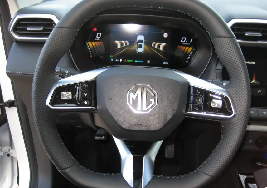 Vue rapprochée du volant noir perforé avec logo MG et tableau de bord numérique du MG ZS 1.5 HYBRID+197 LUXURY blanc 2026.