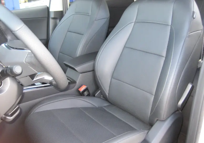 Gros plan sur les sièges avant en cuir noir du MG ZS 1.5 HYBRID+197 LUXURY blanc, avec accoudoir central visible.