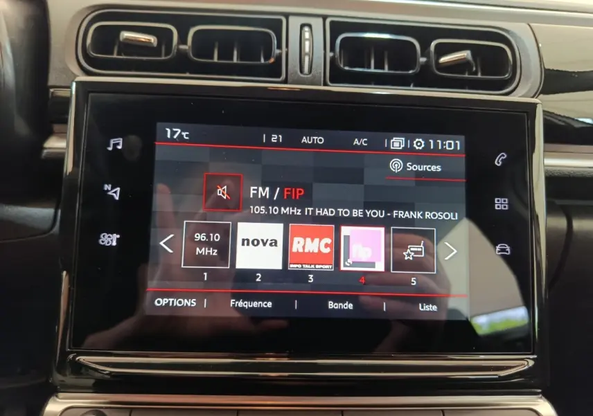 Gros plan sur l'écran tactile central du tableau de bord de la Citroën C3 blanche, affichant la radio FM avec plusieurs stations.