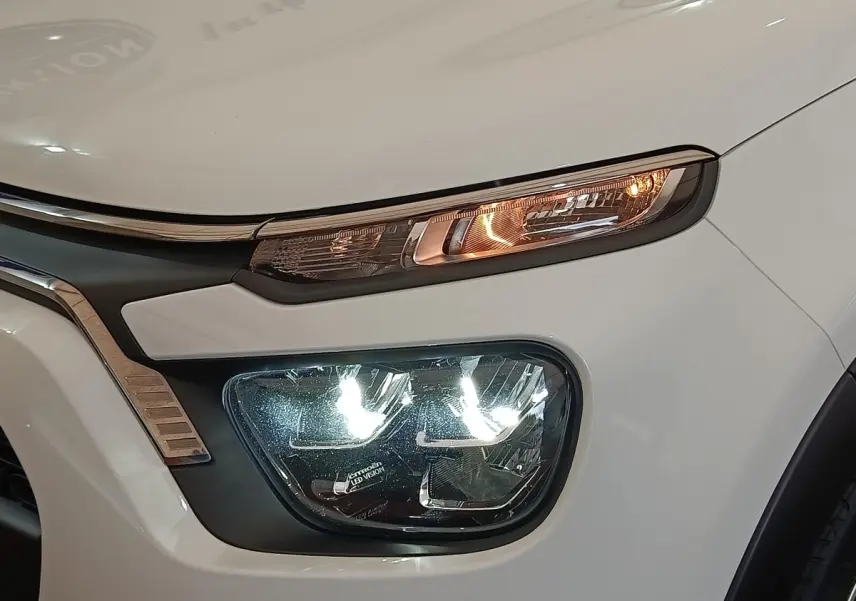 Gros plan sur l'avant droit blanc d'une Citroën C3 2022, mettant en valeur ses phares LED allumés et la calandre chromée.