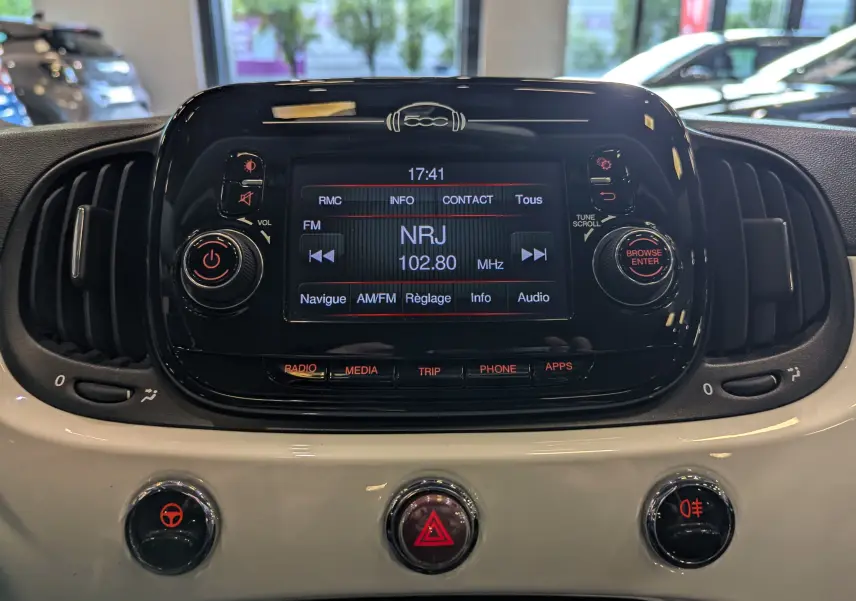 Gros plan sur la console centrale noire et blanche du Fiat 500 Blanc Bossanova avec écran radio affichant NRJ 102.80 MHz.
