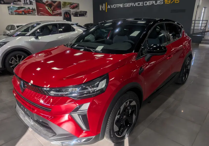 Renault Captur E-Tech hybride rouge flamme avec toit noir, vue 3/4 avant droit en showroom intérieur.