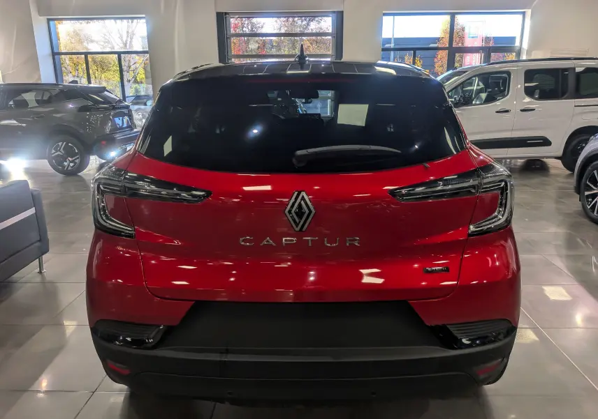 Vue arrière d'un Renault Captur E-TECH 2025 rouge flamme avec toit noir dans un showroom lumineux.