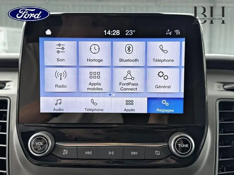 Écran tactile central du Ford Transit Custom blanc, affichant le menu principal du système multimédia avec commandes audio.
