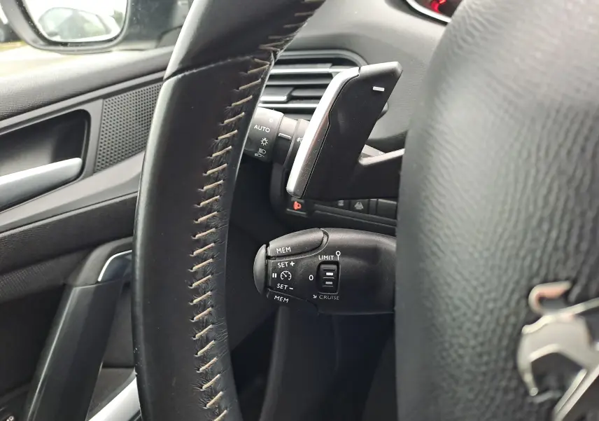 Gros plan sur le volant en cuir noir et les commandes de régulateur de vitesse côté gauche d'une Peugeot 308 gris 2019.