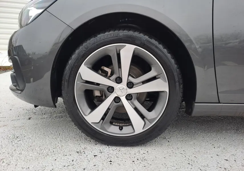 Gros plan sur la roue avant gauche grise d'une Peugeot 308 2019 avec jante alliage à cinq branches.