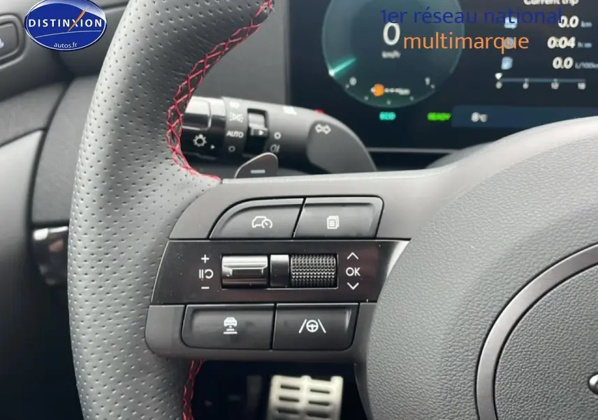 Gros plan sur le volant sport en cuir noir avec surpiqûres rouges du Hyundai Tucson gris écotronique, affichage digital en arrière-plan.