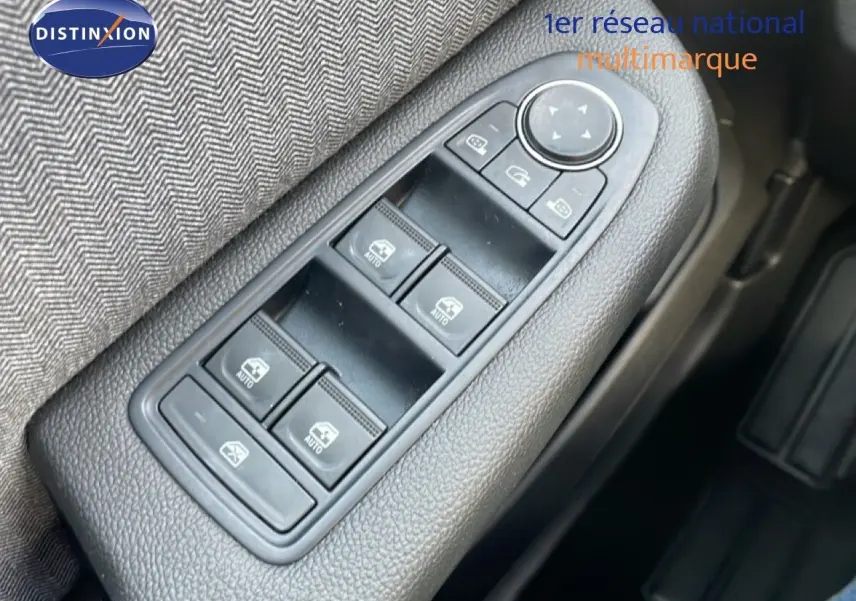 Gros plan sur les commandes de lève-vitres et rétroviseurs côté conducteur d'une Renault Clio rouge Désir Métal 2025.