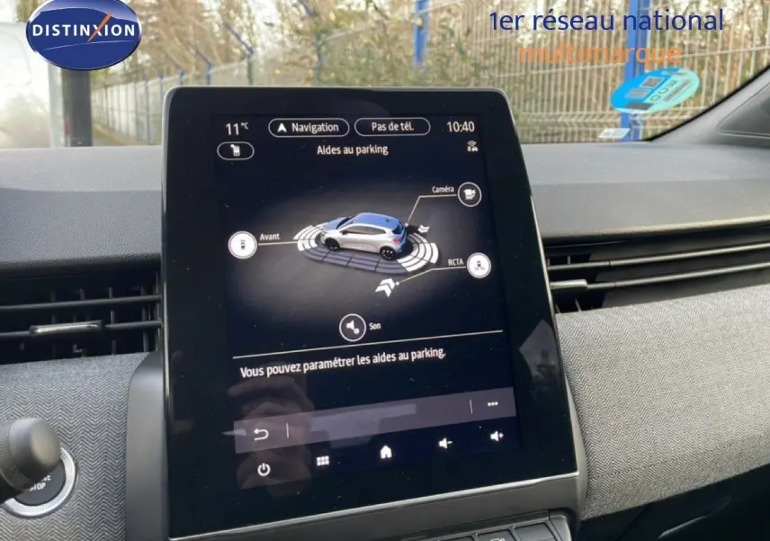 Écran tactile central de la Renault Clio rouge Désir Métal affichant l'aide au parking en intérieur.