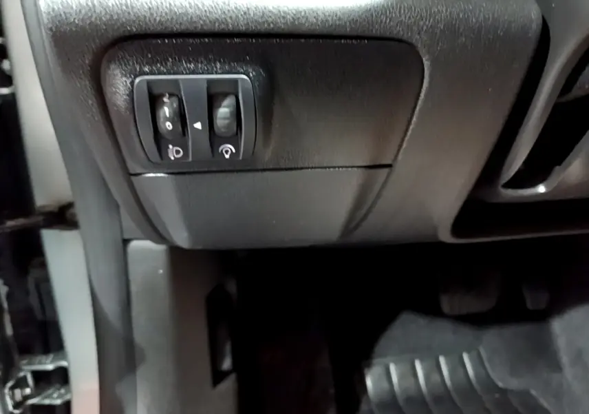 Gros plan sur les commandes de réglage des phares et du tableau de bord côté gauche d’une Renault Mégane Business Blue dCi 115 EDC gris clair.