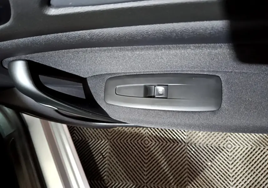 Gros plan sur la commande de lève-vitre électrique côté conducteur de la porte intérieure noire d’une Renault Mégane gris clair.
