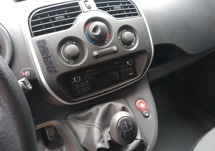 Vue rapprochée du tableau de bord et levier de vitesses manuel d'un Renault Kangoo blanc, avec commandes de climatisation et radio intégrées.