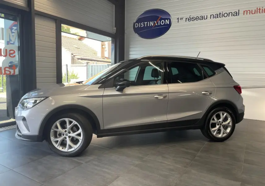 Vue latérale gauche d'un SEAT Arona 2024 gris GRS avec jantes alliage 16 pouces et toit noir en showroom.