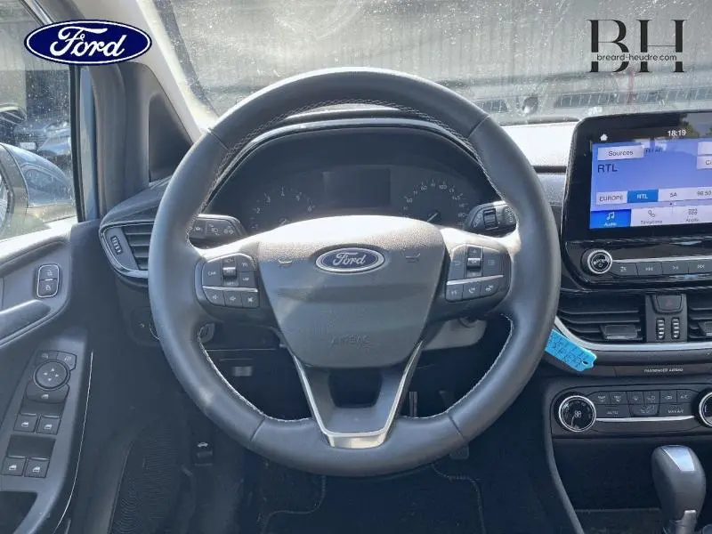 Vue intérieure centrée sur le volant cuir Ford d'une Fiesta 2022 avec tableau de bord et écran tactile noir.