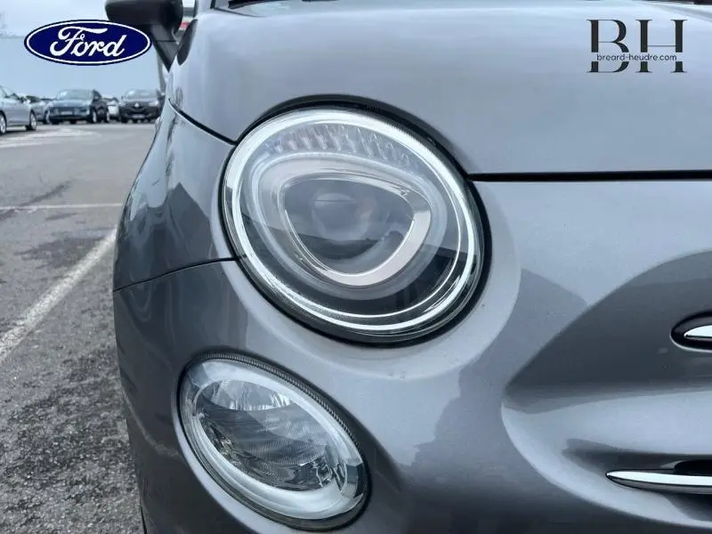 Gros plan sur le phare avant gauche d'une FIAT 500 1.2 8v Lounge gris métallisé avec calandre chromée.