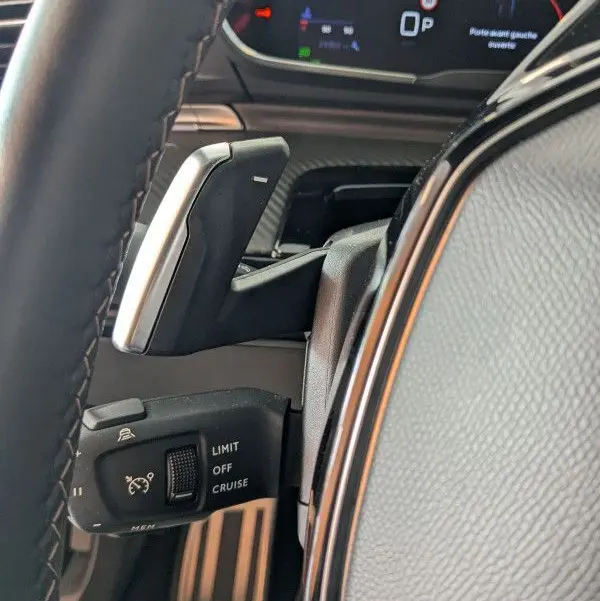 Gros plan sur la commande de régulateur de vitesse et palettes au volant cuir noir du Peugeot 508 SW gris selenium 2024.