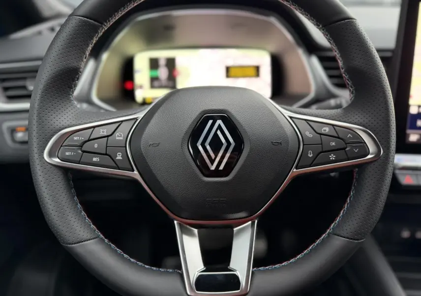 Gros plan sur le volant noir perforé avec surpiqûres bleu blanc rouge du Renault Captur Bleu Iron, tableau de bord numérique flou en arrière-plan.