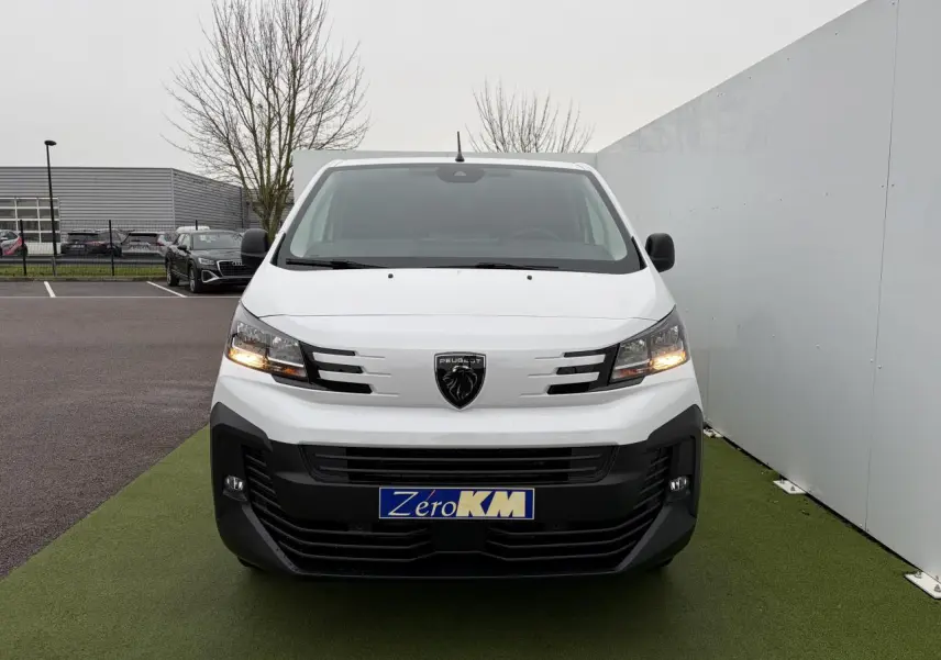 Vue de face du Peugeot Expert Fourgon blanc Icy avec calandre noire et feux allumés sur parking.