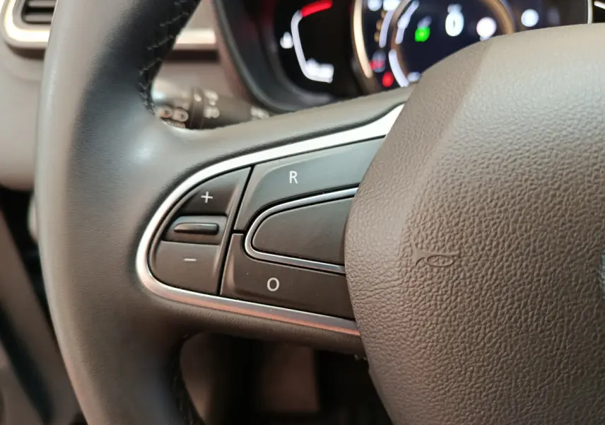 Gros plan sur les commandes du volant noir du Renault Kadjar gris foncé, avec tableau de bord numérique en arrière-plan.