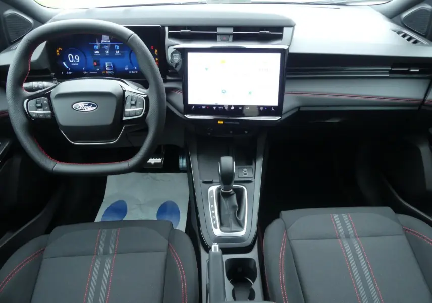 Vue intérieure avant du Ford Puma 2025 avec tableau de bord numérique, écran tactile 12 pouces et surpiqûres rouges sur sièges noirs.