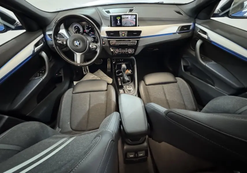 Vue intérieure avant de la BMW X2 bleu, montrant le tableau de bord, volant multifonctions et écran central avec caméra de recul.