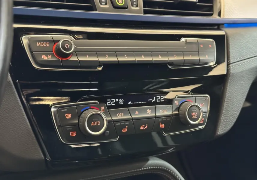 Gros plan sur la console centrale noire du BMW X2 xDrive25e 2021, montrant la climatisation automatique bi-zone et les commandes digitales.