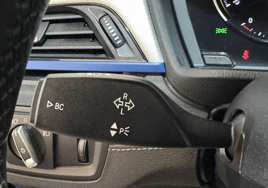 Gros plan sur la manette de clignotant gauche du BMW X2 bleu, avec tableau de bord et aérateur visibles.