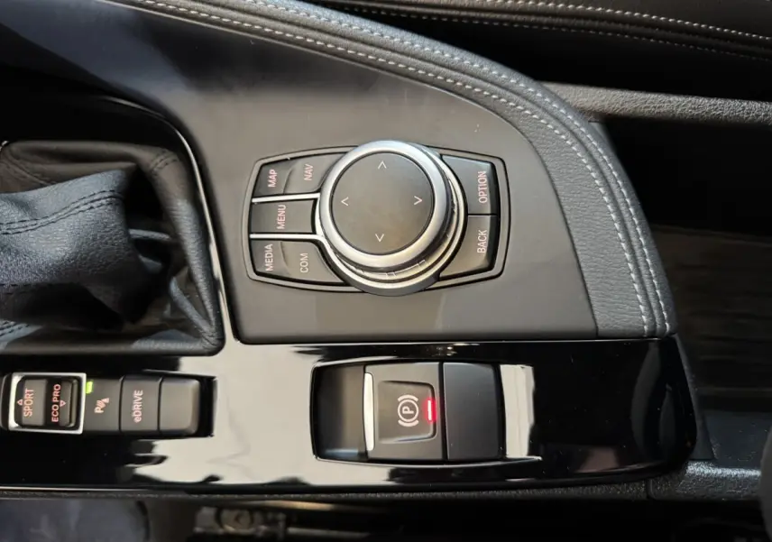 Vue rapprochée de la console centrale noire avec commandes multimédia et frein à main électrique du BMW X2 bleu.
