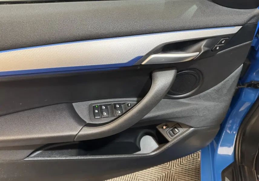 Vue rapprochée de la porte avant gauche bleu électrique du BMW X2 xDrive25e M Sport avec commandes de vitres et poignée noire.