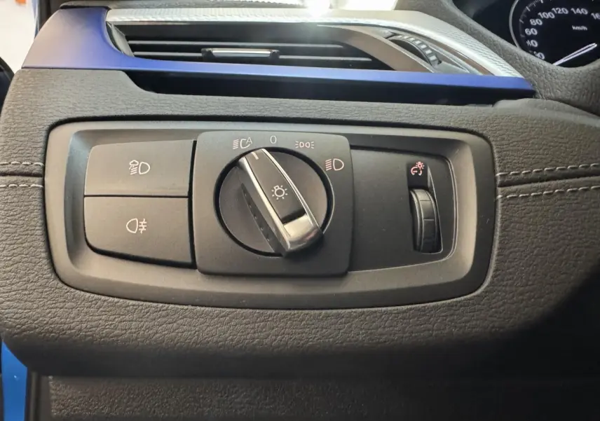 Détail du panneau de commandes d’éclairage sur tableau de bord noir avec insert bleu d’une BMW X2 xDrive25e M Sport 2021.