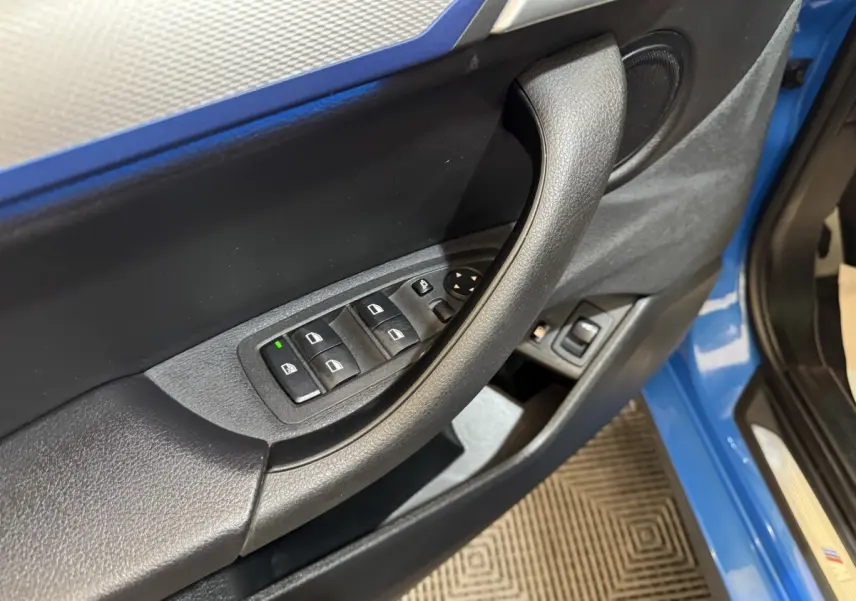 Gros plan sur la porte avant gauche bleu de la BMW X2 xDrive25e, avec commandes électriques des vitres et haut-parleur intégré.