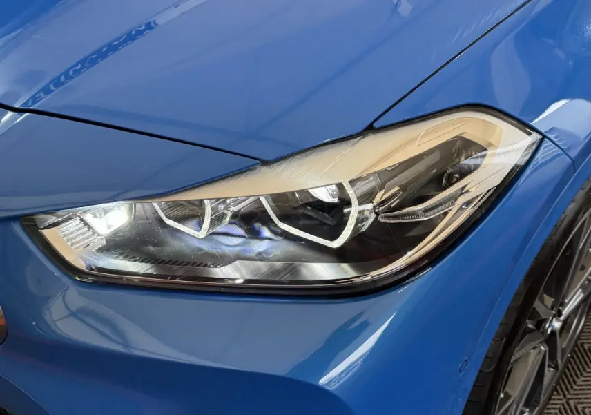 Gros plan sur le phare avant droit bleu vif d'une BMW X2 xDrive25e M Sport 2021, détails LED visibles.
